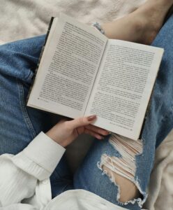 Crop faceless woman reading book on bed